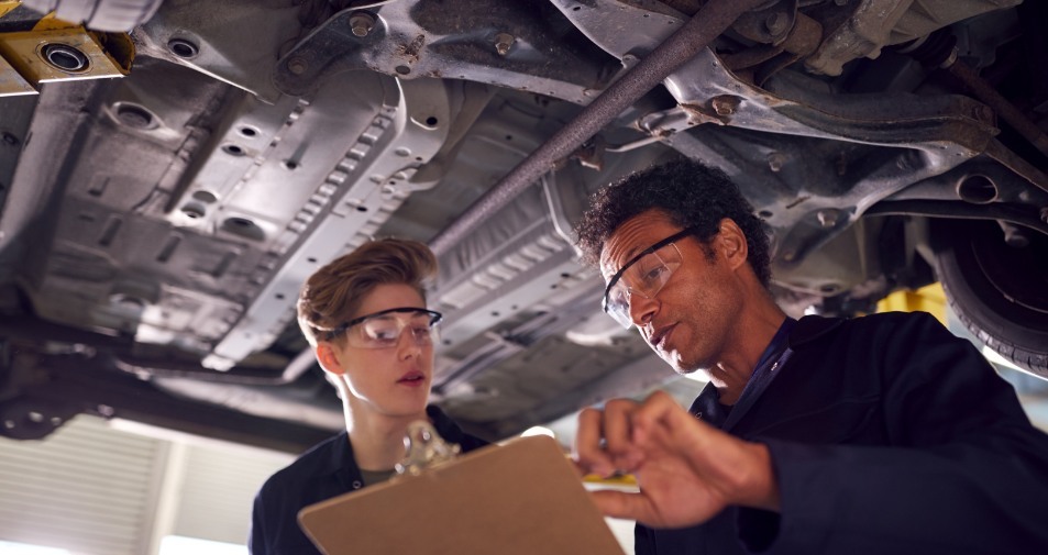 male-tutor-with-student-looking-underneath-car-on--599XJPD