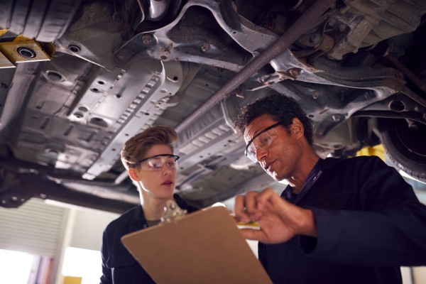 male-tutor-with-student-looking-underneath-car-on--599XJPD